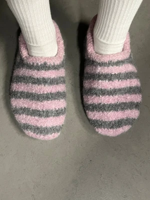 Sailor Slippers - egenstickade & tuvade ulltofflor - Mysiga tofflor i ull med breda ränder i ljusrosa och grått. Modellen är rundad framtill och har en mjuk, fluffig känsla som passar perfekt för hemmabruk. Tofflorna är egenstickade och tovade har en klassisk, enkel design utan synliga detaljer som snörning eller dragkedja.