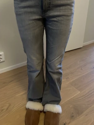 Bootcut jeans i ljusgrå denim - Säljer ett par bootcut jeans i ljusgrå tvättad denim med klassiska fem fickor och dragkedja fram. Jeansen har en lätt utsvängd passform nedtill och raka ben, vilket ger en avslappnad och cool look. Perfekta att matcha med sneakers eller boots.