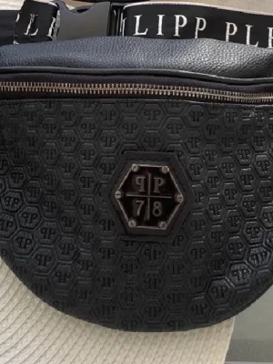 Svart magväska från Philipp Plein - Säljer en svart magväska från Philipp Plein med präglat PP-mönster och metallplakett framtill. Väskan har en grov dragkedja och justerbart band med logotyp. Perfekt för att bära dina viktigaste grejer på ett stilrent sätt.