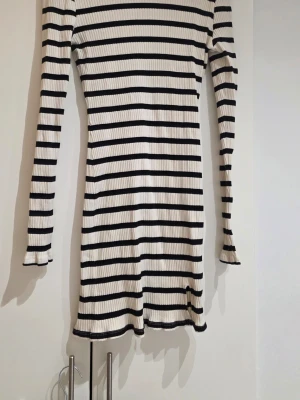 Randig ribbad klänning Gina Tricot - Säljer en ribbad kortklänning från Gina Tricot i storlek L. Klänningen är vit med svarta horisontella ränder, har långärmade ärmar och en figurnära passform. Materialet är mjukt och stretchigt, perfekt för dig som gillar enkel och stilren design.