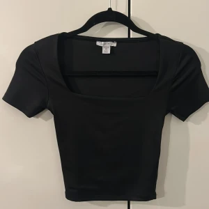 Svart croppad topp från new Yorker  - Säljer en svart croppad topp från new Yorker i storlek XS. Toppen har korta ärmar och en fyrkantig urringning som ger en modern vibe. Materialet är mjukt och stretchigt, perfekt för att styla med jeans eller kjol. Enkel och stilren design.