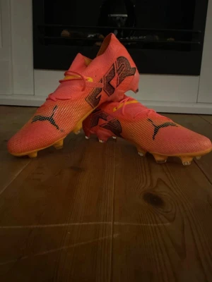 Puma Future 7 Ultimate FG/AG fotbollsskor - Säljer ett par Puma Future 7 Ultimate FG/AG fotbollsskor i en riktigt fet orange färg med gula och svarta detaljer. Skorna har snörning, stickad ovandel och mönstrad sula med dobbar för gräs och konstgräs. Puma-logga på både ovansida och undersida.