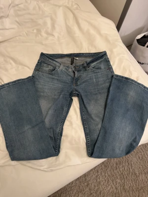 Blå bootcut jeans från Divided - Snygga blå jeans från Divided med klassisk femficksdesign och bootcut-ben. Jeansen har knapp och dragkedja fram samt bakfickor med lock och knapp. Materialet är jeans med en mjuk tvättad finish och subtila slitningar.