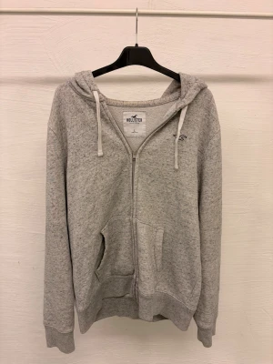 Grå hollister hoddie - Pris går att diskuteras. Grå hollister hoddie med zip och vita snören. Fräsch och perfekt nu till vintern och våren.