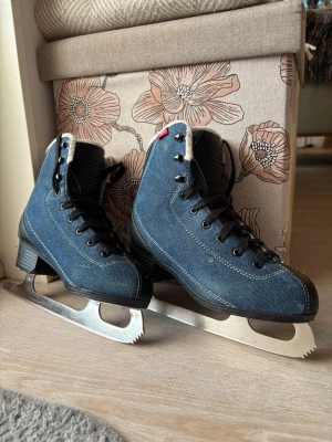 Blå jeans skridskor med svart snörning - Säljer ett par snygga skridskor från Revolution i blå denim-look med svarta detaljer och snörning. Insidan är fodrad med vitt syntetmaterial för extra komfort. Yttermaterialet är robust och har vita sömmar som kontrast. Perfekt för vinterns isäventyr! Ny slipade!