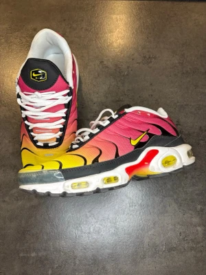 Nike Air Max tn - Säljer ett par Nike Air Max Plus med grym färgskiftning från rosa till gul och svarta detaljer. Skorna har vit sula med synliga Air-enheter i gult och rött, samt vita skosnören. Ovandelen är i syntetmaterial och mesh för bra andningsförmåga. Ikonisk TN-logga på plösen och hälen.