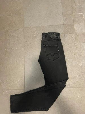 Replay Anbass svarta jeans - Säljer ett par Replay Anbass jeans i svart tvätt med snygga detaljer på bakfickorna och Replay-logga. Jeansen har smal passform och klassisk femficksdesign med dragkedja. Materialet är stretchigt jeans och midjan är normal. Storlek 29/32 men fungerar bra för 30/32 också. De kostar 299kr och köpta för 999kr men väl använda.