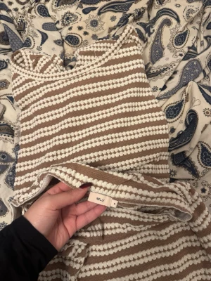 Randig stickad sett från Nelly med tröja och kjol - Superfin stickad klänning från Nelly i beige och vitt med horisontella ränder. Klänningen har smala axelband och ärmlös design, perfekt för varmare dagar. Mjuk och skön kvalitet som känns lyxig och trendig.