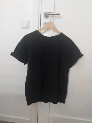 Svart t-shirt från Divided H&M - Enkel svart t-shirt från Divided H&M i storlek S. Klassisk modell med rund halsringning och uppvikta korta ärmar. Perfekt basplagg till garderoben och lätt att matcha med allt.