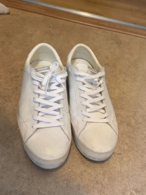 Vita Crime London Distressed Sneakers - Säljer ett par vita sneakers från Crime London med cool distressed look. Skorna har snörning, rund tå och detaljer i mocka på häl och tå. Tillverkade i skinn och mocka för en clean men edgy vibe. Använda 3-4 gånger endast i somras. Stl 44. Box tillkommer!