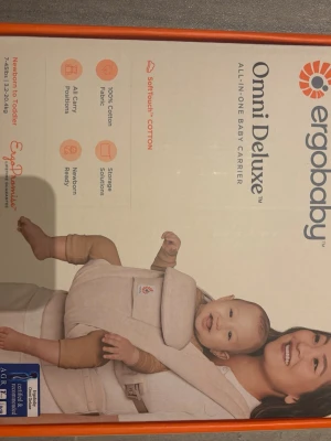 Beige babybärsele Ergobaby Omni Deluxe - Säljer en beige babyväst från Ergobaby, modell Omni Deluxe. Västen är tillverkad i 100% bomull och har flera smarta förvaringsfickor, vadderade axelband och justerbar passform. Perfekt för att bära barnet på olika sätt och har en stilren, enkel design.
