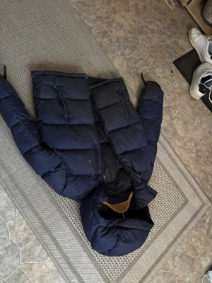 Mörkblå pufferjacka Polo Ralph Lauren - Säljer en mörkblå pufferjacka från Polo Ralph Lauren. Jackan har en hög krage, dragkedja framtill och två bröstfickor med dragkedja. Tillverkad i polyester och perfekt för kalla dagar. Klassisk och stilren design som funkar till det mesta.