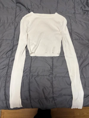 Vit croppad ribbad topp FB Sister - Säljer en vit croppad långärmad topp från FB Sister. Toppen är ribbad och har en enkel, stilren design med rund halsringning. Tröjan har en splitt på båda armarna längst ned