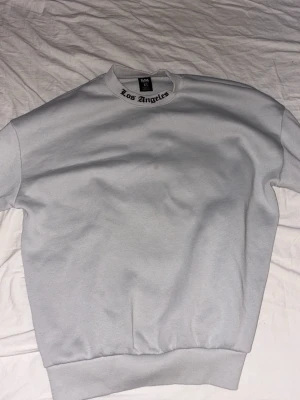 Vit oversized sweatshirt Los Angeles - Säljer en vit oversized sweatshirt från Black Squad i storlek XS. Tröjan har trycket 'Los Angeles' i svart på både kragen och ryggen. Tillverkad i mjuk bomullsmix och har klassisk rund hals och ribbade muddar.