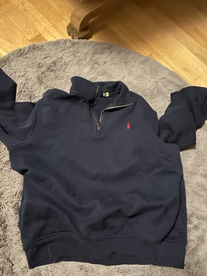 Marinblå half zip tröja Polo Ralph Lauren - Säljer en marinblå långärmad tröja från Polo Ralph Lauren med klass sopig stil. Tröjan har half zip-dragkedja och den ikoniska röda loggan broderad på bröstet. Perfekt till chill eller när du vill se lite extra clean ut. aldrig använd 