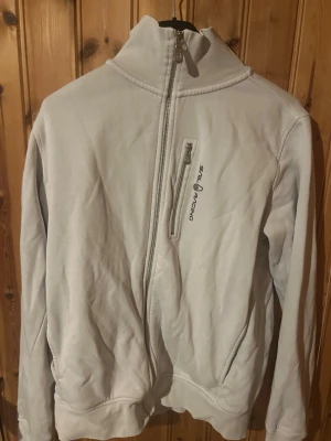 Vit fleecejacka från Sail Racing - Säljer en vit fleecejacka från Sail Racing med hög krage och sned dragkedja. Jackan har en bröstficka med dragkedja och diskret logga på bröstet. Perfekt för kyliga dagar och enkel att matcha med det mesta.