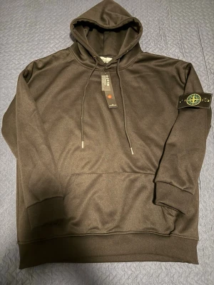 Stone Island Hoodie – Svart, Strl S (sitter som M) - Snygg svart hoodie med klassiska Stone Island-badgen på armen. Tröjan är i storlek S men sitter mer som en M – perfekt för dig som vill ha en lite rymligare passform. Mjuk och bekväm med huva, känguruficka och justerbara snören. Hoodien är oanvänd och ny. Passar både till vardags och för en mer street-inspirerad look. Snabb affär uppskattas!
