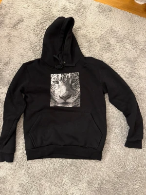 Hoodie från the cool elephant - Stilren svart hoodie med ett coolt leopardmotiv framtill. Mjuk och bekväm passform med huva och magficka. Använd fåtal gånger och i mycket fint skick, inga tydliga slitningar eller fläckar. Perfekt till vardags eller för en streetwear-look. 