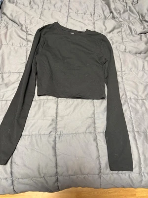 Svart croppad långärmad topp 157 - En enkel och stilren svart croppad topp från 157 i storlek XS. Toppen har långa ärmar och är gjord i mjuk bomull med lite stretch för skön passform. 
