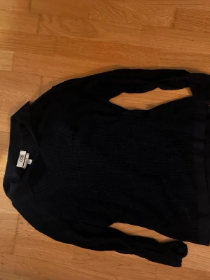Svart stickad tröja från COS - Säljer en svart stickad tröja från COS med klassisk krage och lång ärm. Tröjan har en diskret struktur i materialet och en stilren look som passar perfekt till jeans eller kjol. Enkel och clean design för dig som gillar minimalistiskt mode.