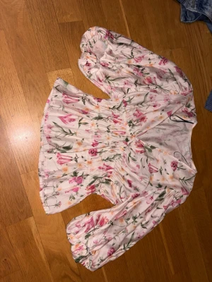 Blommig blus från H&M med puffärm - Supersöt blommig blus från H&M i storlek S. Blusen är vit med rosa och gröna blommor, har bred smock i midjan och puffiga långärmar med resår vid ärmslut. V-ringad och lätt utsvängd nertill, perfekt för vår och sommar. Har använt 1 gång 
