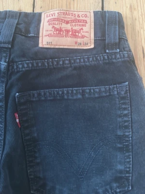 Levi's 511 svarta manchesterbyxor - Säljer ett par svarta Levi's 511 manchesterbyxor med klassisk femficksdesign och raka ben. Byxorna har snygga detaljer som präglad knapp och det ikoniska läderpatch bak i midjan. Perfekta för dig som gillar en tidlös och clean look.