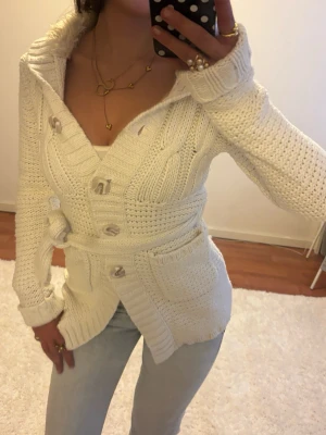 Vit stickad kofta med huva och bälte - Mysig vit stickad kofta med stora knappar, fickor framtill och bälte i midjan o päls i huvan. Går att använda utan bältet. Jag är 168 och det är mina bilder, köp via köp nu direkt eller Swish, kvar tills markerad som såld 💖 