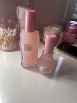 Glow Watermelon toner och face mist - Säljer två produkter från Glow: en Watermelon Hydrating Skin Tonic i en vågformad glasflaska med rosa lock (120 ml) och en Watermelon Glow Niacinamide Face Mist i rund glasflaska med rosa lock. Båda har en ljusrosa färg och ger en fräsch känsla till huden.