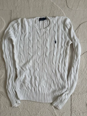 Vit kabelstickad tröja Polo Ralph Lauren - Helt ny! Använd 2-3 gånger.Kabelstickad vit tröja från Polo Ralph Lauren i storlek XS. Klassisk rund halsringning, långärmad och med den ikoniska mörkblå loggan broderad på bröstet. Tröjan är ribbad vid ärmslut och nederkant och har en riktigt clean och tidlös look.