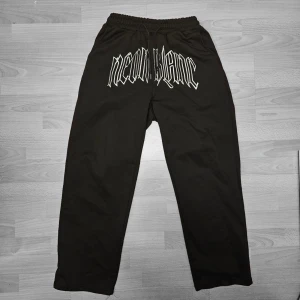 Svarta mjukisbyxor Neon Blanc S - Svarta mjukisbyxor från Neon Blanc i storlek S. Byxorna har resår i midjan och ett stort vitt tryck framtill med märkesnamnet i coolt typsnitt. Perfekta för chill dagar eller streetwear-stil. Tillverkade i mjukt material för maximal komfort.