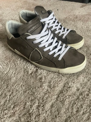 Philippe Model grå sneakers i skinn - Snygga sneakers från Philippe Model i grått skinn med vita detaljer och vita snören. Klassisk låg modell med rund tå och vit sula. Märkets logga på plösen och sidan. Perfekta för dig som gillar stilrena och exklusiva sneakers. Box kommer med.