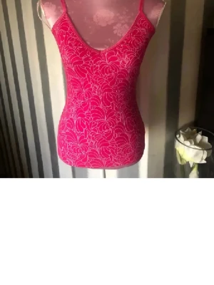 Rosa blommig linnetopp - Säljer en snygg rosa linnetopp med tunna axelband och blommigt mönster i vitt. Toppen har en figurnära passform och är perfekt för varma dagar. Materialet känns mjukt och följsamt mot huden.med inbyggd bh