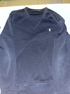 Mörkblå sweatshirt från Polo Ralph Lauren - Klassisk mörkblå sweatshirt från Polo Ralph Lauren med rund halsringning och den ikoniska vita broderade loggan på bröstet. Tröjan har långa ärmar och är tillverkad i mjuk bomull för en skön och avslappnad look. Storlek S utan defekter! Finns fler kläder på min profil!