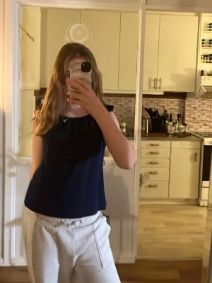 Mörkblå ärmlös linnetopp - Säljer en stilren mörkblå linnetopp med rund halsringning och volangdetaljer vid axlarna. Toppen är ärmlös och har en rak passform som ger en avslappnad look. Perfekt att matcha med både jeans och kjol för en enkel men snygg outfit.