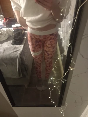 Rosa camonmöstrade  leggings - Säljer ett par snygga leggings i rosa och lila camomönster med vit bred midjeresår och vit detalj på låret. Tight passform och stretchigt material som sitter skönt på kroppen. Perfekta för träning eller chill.
