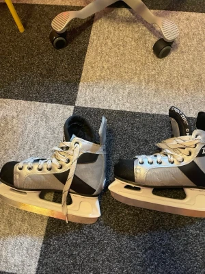 Point zero skridskor  - Säljer ett par skridskor från Point Zero i svart och silver med vita snören och robust design. Skridskorna har högt skaft, vadderad plös och tå, samt slitstarka material. Perfekta för dig som vill åka skridskor med stil.