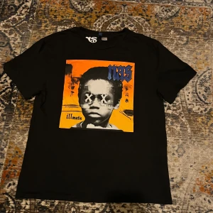 Svart Nas t-shirt med tryck - Svart t-shirt från Nas med ikoniskt färgstarkt tryck på bröstet i orange, blått och gult. Klassisk passform med rund hals och korta ärmar. Perfekt för dig som gillar streetwear och musikvibbar. Materialet är mjukt och skönt bomull. Fint skick storlek Medium