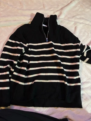  stickad tröja Zara - Säljer en svart stickad tröja från Zara i storlek S med vita ränder. Tröjan har hög krage med half zip-dragkedja och slits nedtill