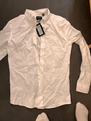 Vit skjorta från Only & Sons - Klassisk vit skjorta från Only & Sons med krage och knäppning framtill. Skjortan har lång ärm och är tillverkad i mjuk bomull som känns skön mot huden. Perfekt att styla med jeans eller chinos för en clean look.