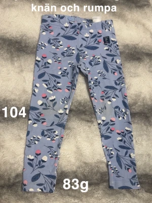 Blommiga leggings i blått  - Supersöta leggings med blommigt mönster. Byxorna har en mjuk resår i midjan och är gjorda i stretchigt material som är skönt att ha på sig. Perfekta för dig som gillar färg och mönster!🌸 Väl använda och missfärgade på knän och rumpa. Kan finnas någon svag fläck som jag missat. Storlek 104 