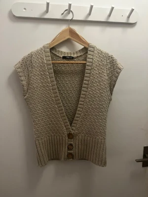 Beige stickad kofta från Jane Norman - Säljer en beige stickad kofta från Jane Norman med korta ärmar och djup v-ringning. Koftan har ett snyggt strukturmönster, bred ribbad kant nedtill och tre dekorativa knappar framtill. 💖💖