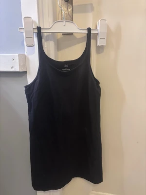 Svart linnetopp från H&M Basic - En enkel svart linnetopp från H&M Basic i ekologisk bomull. Modellen har smala axelband och rak passform, perfekt till sommaren eller som lager under andra plagg. Stilren och lättmatchad för alla tillfällen.