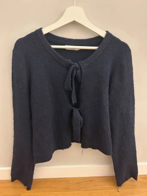 Mörkblå stickad kofta med knyt - Mysig mörkblå stickad kofta från NA-KD med två knyt framtill. Koftan har lång ärm och en croppad passform som ger en avslappnad vibe. Perfekt att slänga över en topp under kyliga dagar.