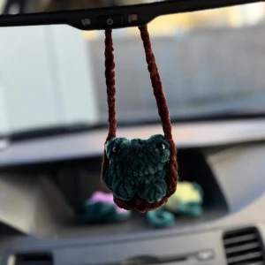 Virkat bilhänge - En virkad groda som passar perfekt att hänga i bilen men självfallet även på andra ställen. Hänget är virkad i mörkgrönt och brunt fluffigt garn vilket gör den väldigt mysig 🐸 Gosedjuren lämpar sig inte för små barn då ögonen är känsliga och kan falla av om man ej är försiktig.