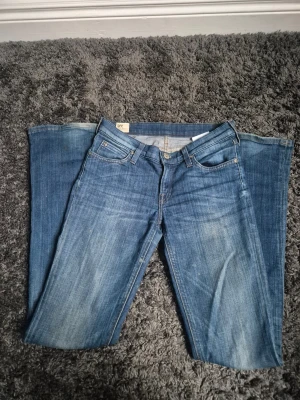 Blå Lee jeans flare - Snygga blå jeans från Lee med klassisk femficksdesign och flare. Jeansen har en mörkblå tvätt med lätt slitningar och Lee-logga på bakfickan samt svart läderpatch i midjan. Perfekt för dig som gillar en tidlös och avslappnad look.
