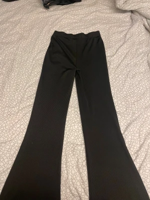 Svarta ribbade bootcut-byxor lager 157 - Svarta ribbade byxor från lager 157 i storlek S. Byxorna har bootcut-modell med utsvängda ben och elastisk midja. Materialet är stretchigt och ger en snygg passform. Perfekta för dig som gillar en trendig och bekväm stil. Lappen sitter lite löst, och jag skulle säga att dom passar jättebra på Medium också