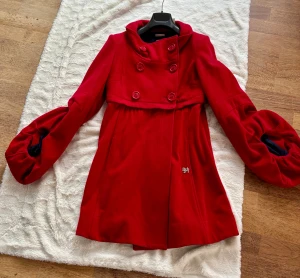Röd kappa från Miss Sixty med puffärm - Säljer en röd kappa från Miss Sixty med unika puffärmar och dubbelknäppning framtill. Jackan har en snygg krage, markerad midja och mörkblått foder. Perfekt för dig som vill sticka ut med en cool och färgstark look. Jackan har ett blixtlås i midjan som möjliggör att den kan användas som en kort jacka för variation. (2 olika jackor i ett). Köpt på miss sixty butik i Milano . Nypris över 5000 sek