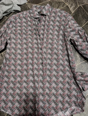 Mönstrad skjorta från Finest Shirtmakerstl L - Säljer en långärmad skjorta från Finest Shirtmaker i regular fit. Skjortan har ett detaljerat mönster i svart, rött och vitt och är tillverkad i 100% bomull. Klassisk krage och knäppning framtill. Perfekt för dig som gillar att sticka ut med snygga prints. Fint skick