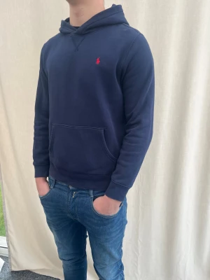 Marinblå hoodie från Polo Ralph Lauren - Snygg marinblå hoodie från Polo Ralph Lauren i storlek som sitter som storlek S-M beror på hur du själv vill att den ska sitta. Jag själv är 184 cm