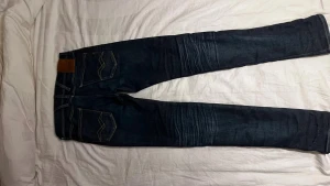 Replay Hyperflex Anbass  - Snygga Replay Hyperflex Anbass jeans i mörkblå tvätt med klassiska fem fickor och kontrastsömmar. Stretchigt material för extra komfort och smal passform. Läderpatch med Replay-logga bak i midjan. Perfekt för dig som gillar stilrena och moderna jeans.